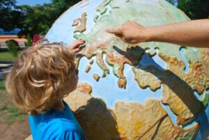 A person and a child pointing to Europe on a big globe