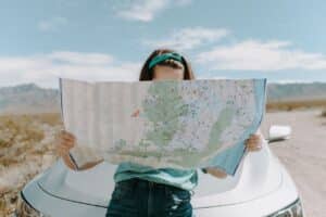 A girl in front of a white car, looking at a map.