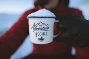 A person holding “The adventure begins” mug in snow showing that becoming an expat is right for you.